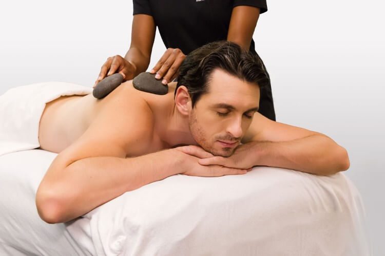 Person lying down with eyes closed, receiving a back massage using smooth stones.